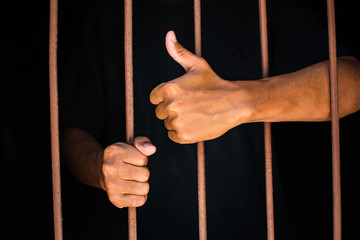 hand man thumbs up and hold steel in jail on black background.concept for prisoner,happy,detain,funny