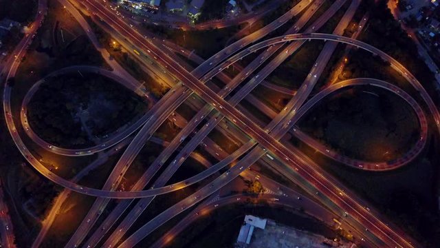 4K. Aerial view of road interchange or highway intersection with busy urban traffic speeding on the road at night. Junction network of transportation taken by drone.