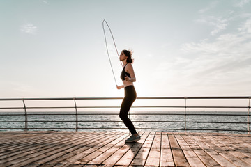 fit teenage girl with jump rope on a beach exercising and working out - obrazy, fototapety, plakaty