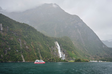Boat cruising to waterfall at Milford Sound New Zealand