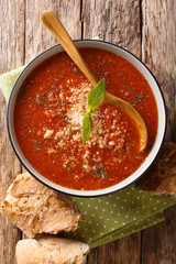 Thick tomato basil cream soup with parmesan cheese close-up in a bowl with bread. Vertical top view