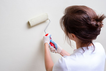 a woman makes repairs in the apartment. She paints the walls with a paint roller. she's wearing a white t-shirt.