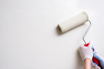 a woman's hand in a construction glove holds a paint roller against a light colored wall