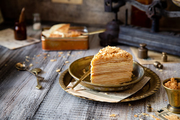 tasty slice of homemade creamy layered traditional russian cake napoleon on vintage gold metal plates on grey wooden table with old scales
