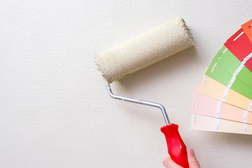 the painter holds the paint roller against the light wall and the color samples. the concept of repair in the apartment and painting the walls