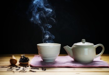 a cup of hot tea with tea pot , hot smoke, dark background.