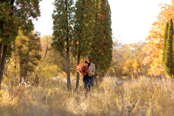 Woman autumn portrait. Cute girl outdoors with a bouquet of yellow maple leaves in the forest, autumn fall concept. Young girl in autumn forest.