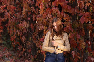 Portrait of a young girl in a leather jacket in the autumn Park on a background of red leaves. Colorful autumn nature. A young woman walks in the autumn forest.