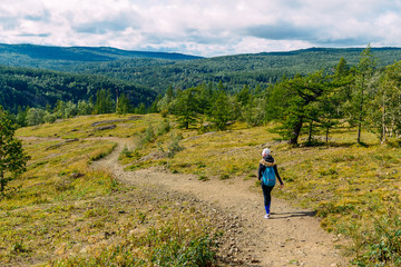 Obraz premium Woman with backpack walks along footpath with mountain