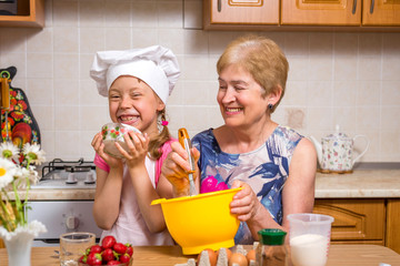Grandmother and little granddaughter prepare the dough for the cake.