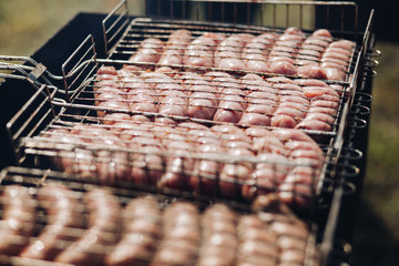 Heap of fresh appetizing sausage cooking on barbecue grill ready for outdoor picnic top view. Close-up juicy grill meat product during preparing on charcoal at sunny summer day