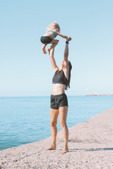 Fototapeta na wymiar Young fit woman mom with little cute girl exercising on the beach together, healthy lifestyle, dynamic gymnastic