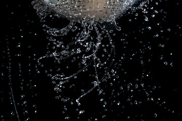 Flow and drops of water through holes in a colander on a dark background - obrazy, fototapety, plakaty