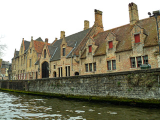 Fototapeta na wymiar Brick buildings near canal in Bruges, Belgium. Beautiful urban scene and cityscape of medieval architecture. View with the old facade of houses in the ancient European city Brugge.
