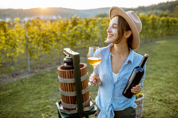 Young and cheerful woman tasting wine, while standing near the press machine on the vineyard on a...