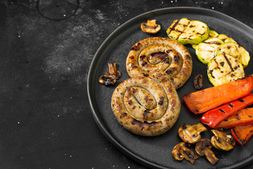 Grilled sausages on a black plate on a dark background