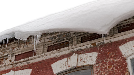 A huge snow block dangerously hangs down from the building karziz, ready to break and fall down.