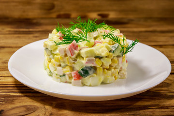 Salad with crab sticks, sweet corn, cucumber, eggs and mayonnaise on wooden table