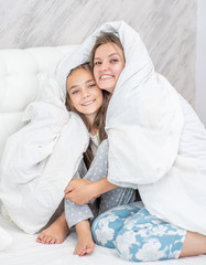 Smiling girl and her young mother enjoy morning at home. Family playing under blanket on the bed in the bedroom