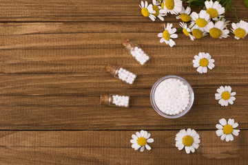 Homeopathic globules and glass bottle on a wooden natural background next to medicinal chamomile flowers.
