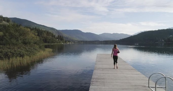 Woman Walking Down A Dock With Yoga Mat At Sunrise