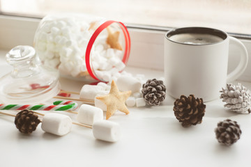 Obraz na płótnie Canvas Cup of hot Chocolate drink with marshmallows, cinnamon sticks, anise star, gift and cones on white background. Winter christmas holiday background.