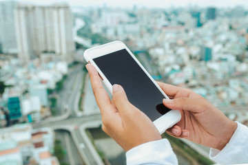 Female hand holding, using smartphone on cityscape with high rise