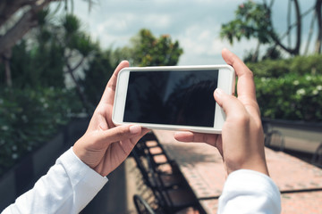 Mockup of female hands holding frameless cellphone with blank screen and making selfie at isolated background.
