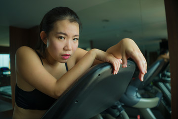 young attractive and fit Asian Chinese woman exhausted during running workout at hotel gym or fitness club jogging in treadmill training hard with tired face expression