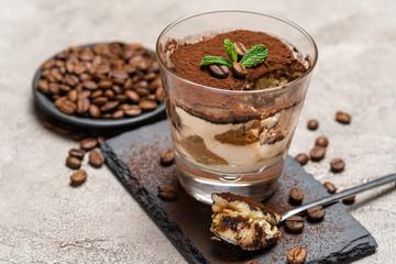 Portion of Classic tiramisu dessert in a glass cup on stone serving board on concrete background
