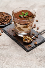 Portion of Classic tiramisu dessert in a glass cup on stone serving board on concrete background