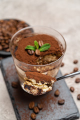 Portion of Classic tiramisu dessert in a glass cup on stone serving board on concrete background