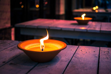 The row of oil lamps flaming at night on the wooden tables, close up. Romantic restaurant exterior.