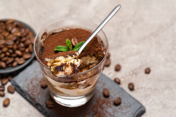 Portion of Classic tiramisu dessert in a glass cup on stone serving board on concrete background