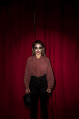 Woman dressed as a clown standing in front on a curtain