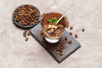 Portion of Classic tiramisu dessert in a glass cup on stone serving board on concrete background