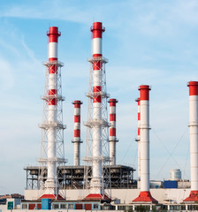 Red and white striped pipes of a city gas power station against a clear sky.