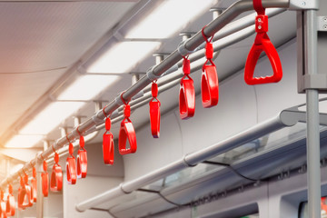 Red handrails on the ceiling bracket in the commuter train. Hanging transport handrail, safety equipment.
