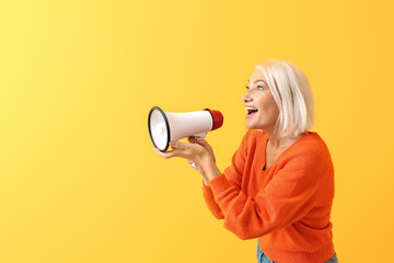 Mature woman with megaphone on color background