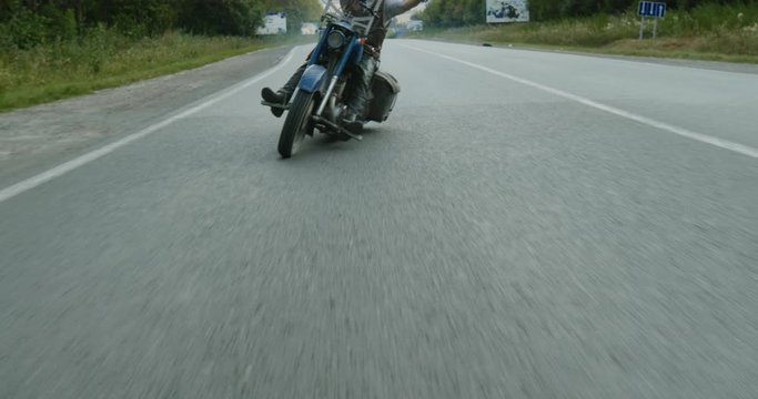 Tracking shot of adult man swerving while riding custom motorbike along asphalt road in countryside