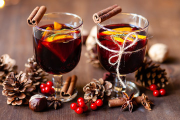 Composition with two glasses of hot mulled red wine with spices. Holiday atmosphere, christmas ligths on dark background. Rustic style, cones, nuts, anise, cinnamon, orang, berries as festive decor 