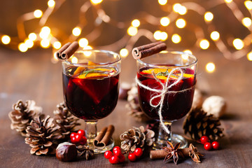 Composition with two glasses of hot mulled red wine with spices. Holiday atmosphere, christmas ligths on dark background. Rustic style, cones, nuts, anise, cinnamon, orang, berries as festive decor 