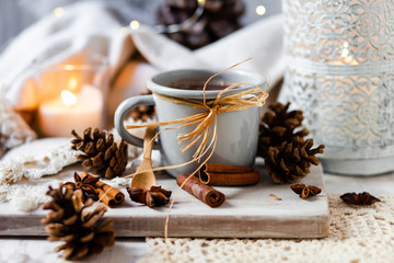 Christmas party rustic decor: grey metal mug with hot chocolate served on wooden board. Candle and delicate lamp, cones, anise stars and cinnamon sticks as decor. Cozy home atmosphere, family time