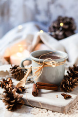 Christmas party rustic decor: grey metal mug with hot chocolate served on wooden board. Candle and delicate lamp, cones, anise stars and cinnamon sticks as decor. Cozy home atmosphere, family time