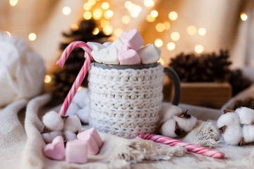 Holiday christmas composition with mug in knitted white sweater with strong hot coffee and marshmallows. Rustic decor, cotton, cones, cinnamon, anise. Lights on. Cozy quite romantic atmosphere