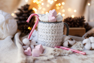 Fototapeta na wymiar Holiday christmas composition with mug in knitted white sweater with strong hot coffee and marshmallows. Rustic decor, cotton, cones, cinnamon, anise. Lights on. Cozy quite romantic atmosphere