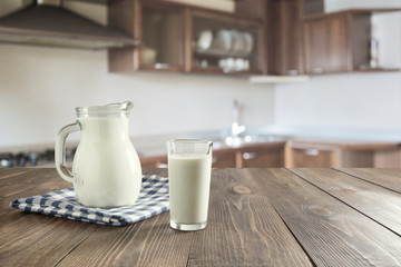 Glass of fresh milk and jug on wooden tabletop with blur kitchen as background.
