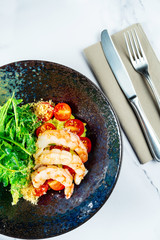 Salad with shrimp, guacamole, arugula and cherry tomatoes in a stylish dark bowl on a marble table with white wine. Seafood salad. Food photo for menu or recipe. Top view, flat lay