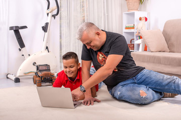 Shot of a father and son browsing on a laptop together  sitting on the floor in their home.