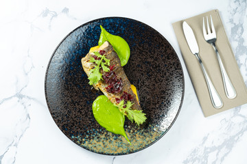 Grilled trout with caramelized beets and green puree on a black plate on a marble table. Seafood. Meal with fish. Food photo for menu or recipe.